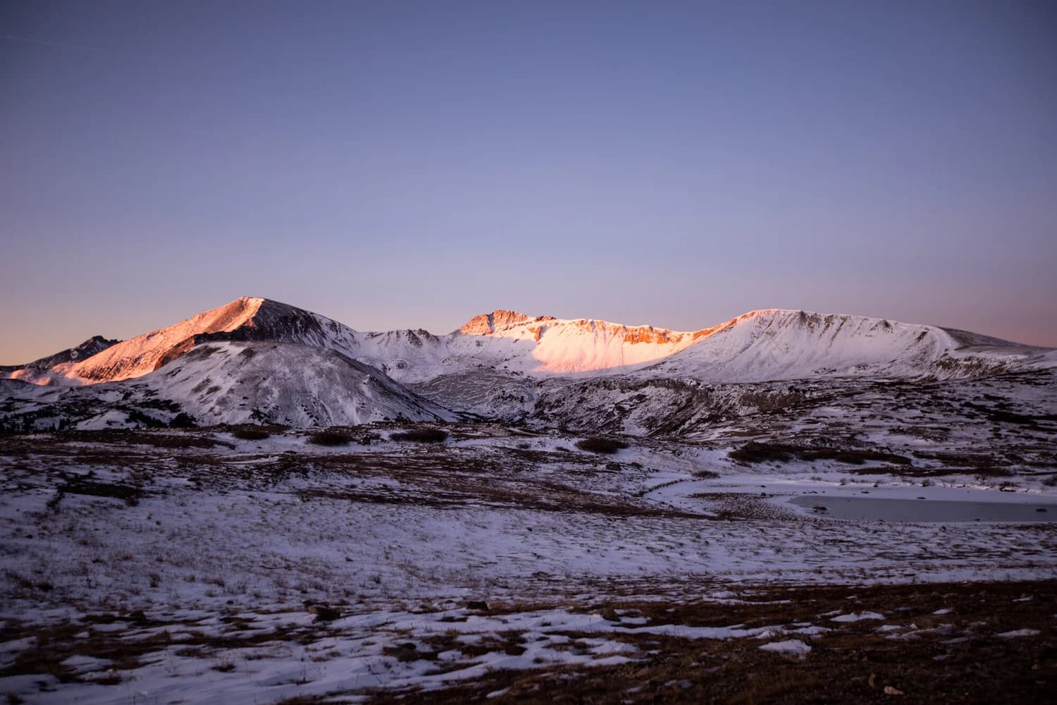 Snow-dusted mountain peaks catching pink alpenglow at sunrise